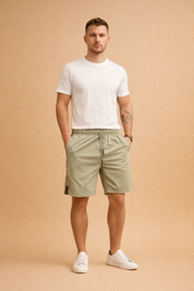 Light sage green lightweight woven men’s summer shorts with elastic waistband and drawstring, smooth matte fabric texture, paired with a clean solid white short-sleeve crew neck t-shirt and minimalist white low-top sneakers for a modern casual look.