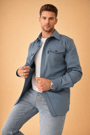 Men’s tailored long-sleeve overshirt with structured collar, front button closure, and dual chest flap pockets, layered over a clean fitted crew-neck top and paired with slim straight-leg denim trousers for a refined casual look.