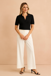Black cable-knit short sleeve polo top paired with tailored wide-leg ivory trousers and black heeled sandals, styled in a chic and modern fashion.