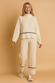 Two-piece beige knit lounge set featuring a relaxed mock-neck sweater with wide sleeves and coordinating wide-leg pants, both detailed with slim black piping lines.