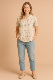 Short-sleeve blouse with a round collar, showcasing a soft cream fabric base detailed with a delicate multicolor floral vine print in pink, blue, yellow, and green.