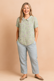 Short-sleeve button-up blouse with a rounded collar, featuring a light green leafy vine pattern and delicate lavender floral print on a light beige base.