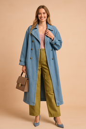 Light blue oversized denim trench coat with gold buttons, styled over a pastel pink ruched top and olive green cargo pants with large utility pockets. Finished with pointed-toe blue heels and a structured taupe handbag.