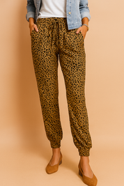 Leopard print jogger pants in golden-brown with black spots, featuring a tapered ankle cut, elastic waistband with drawstring, and side pockets.