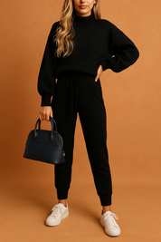 Sleek black knit sweater and jogger co-ord with drawstring waist and ribbed cuffs, styled with a structured navy handbag and classic white sneakers for a polished casual look.