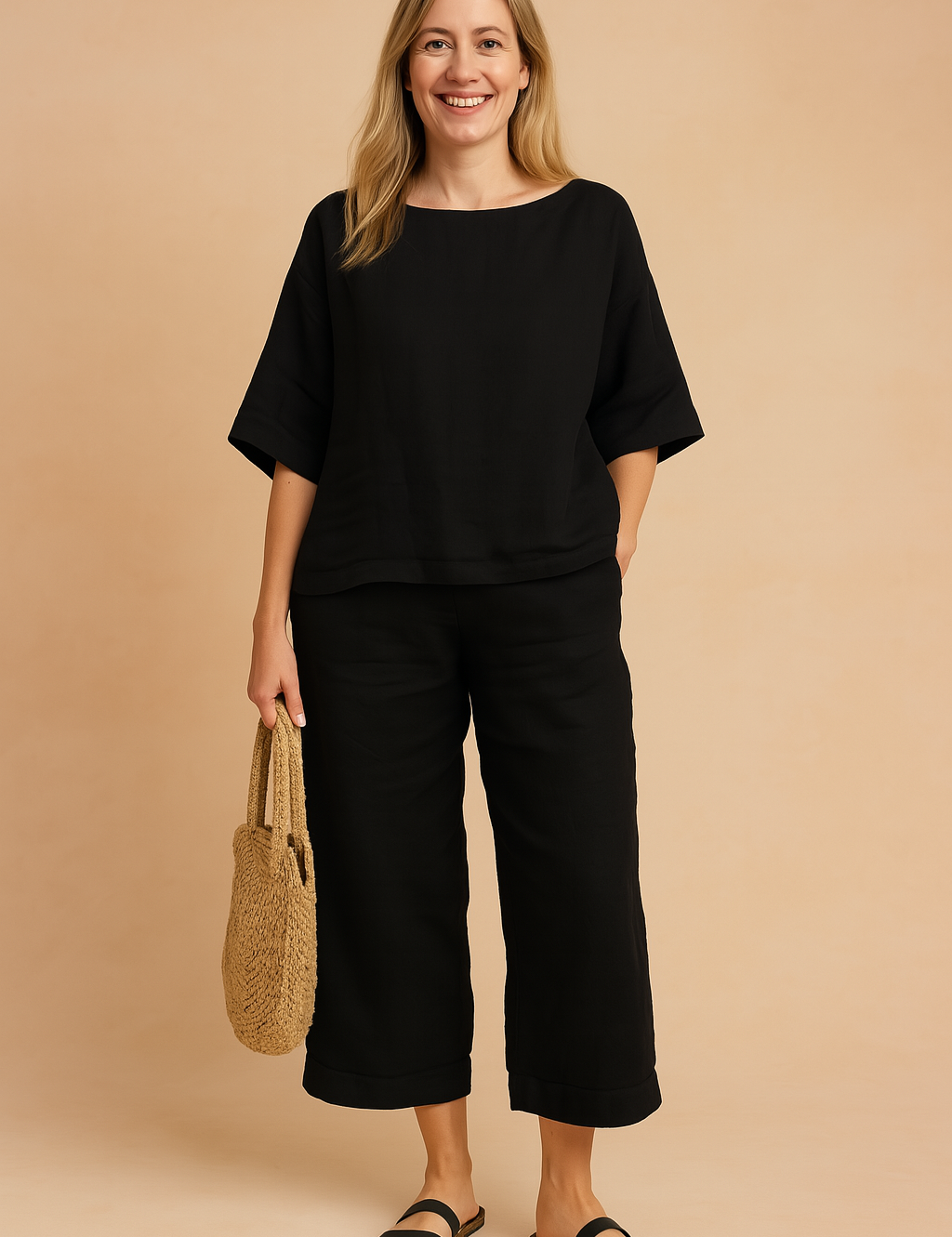 Black linen two-piece set featuring a relaxed-fit elbow-sleeve top and matching cropped pants with a folded hem, styled with black sandals and a woven straw handbag.