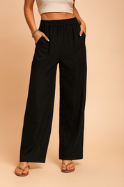 Black wide-leg linen pants with front patch pockets and an elastic waistband, styled with tan flat sandals for a casual-chic look.