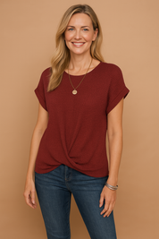Textured burgundy waffle-knit blouse with rolled short sleeves and a front twist hem, paired with medium-wash jeans for a casual yet polished look.
