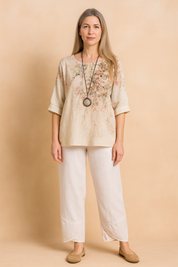 Two-piece linen blend summer outfit featuring a loose, elbow-sleeve cream top with a delicate pink and green floral print and round neckline, paired with white ankle-length pants with cross-panel hems and an elastic waistband.