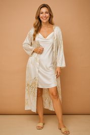Two-piece satin sleepwear set featuring a white mini slip dress with a draped neckline, layered under a lightweight full-length robe adorned with soft beige and gold botanical floral patterns, styled with matching beige slide sandals.
