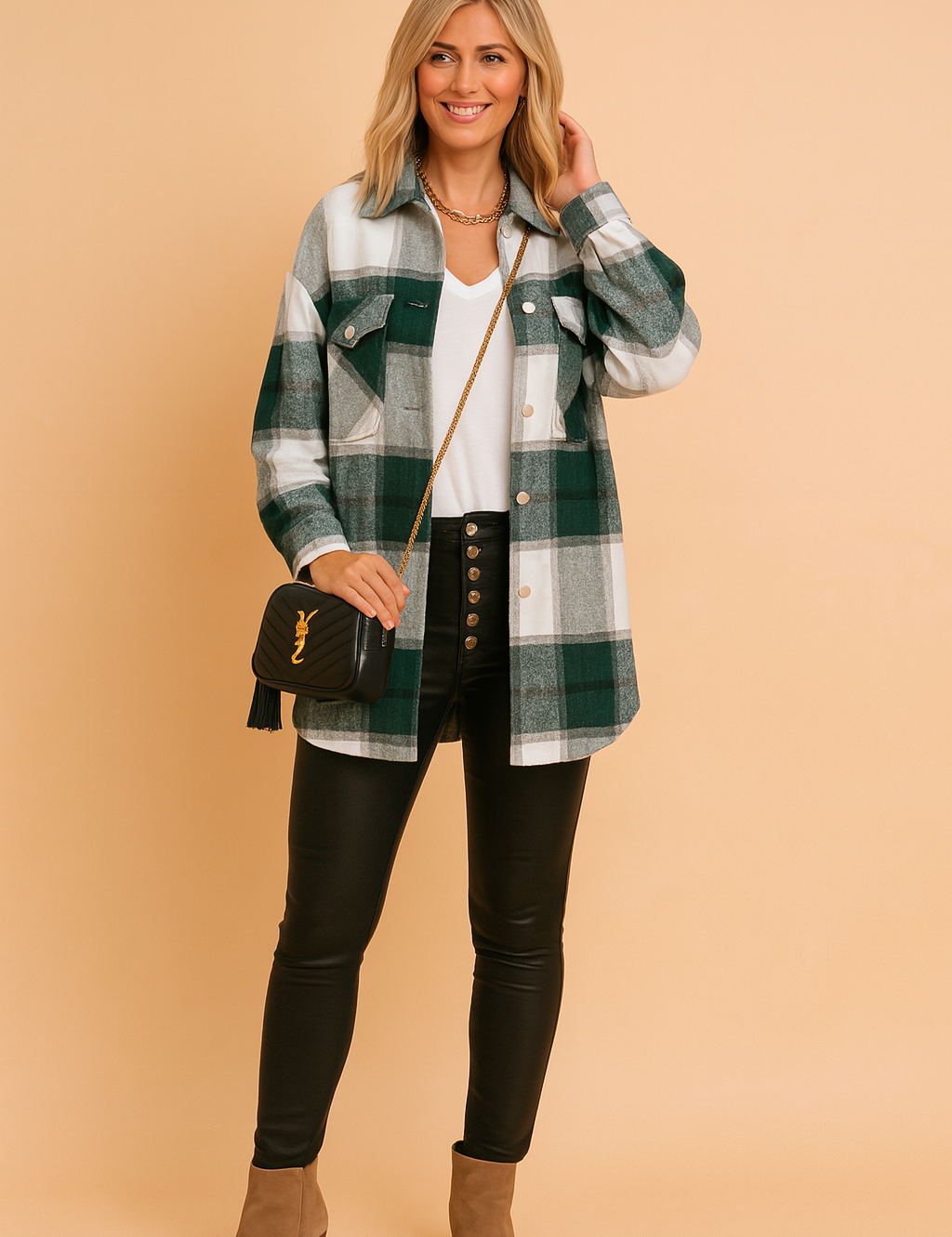 Women's oversized green and grey plaid shacket with dual chest pockets, styled over a white V-neck top and black high-rise leather pants with silver button detailing, completed with tan suede ankle boots and a black crossbody bag.