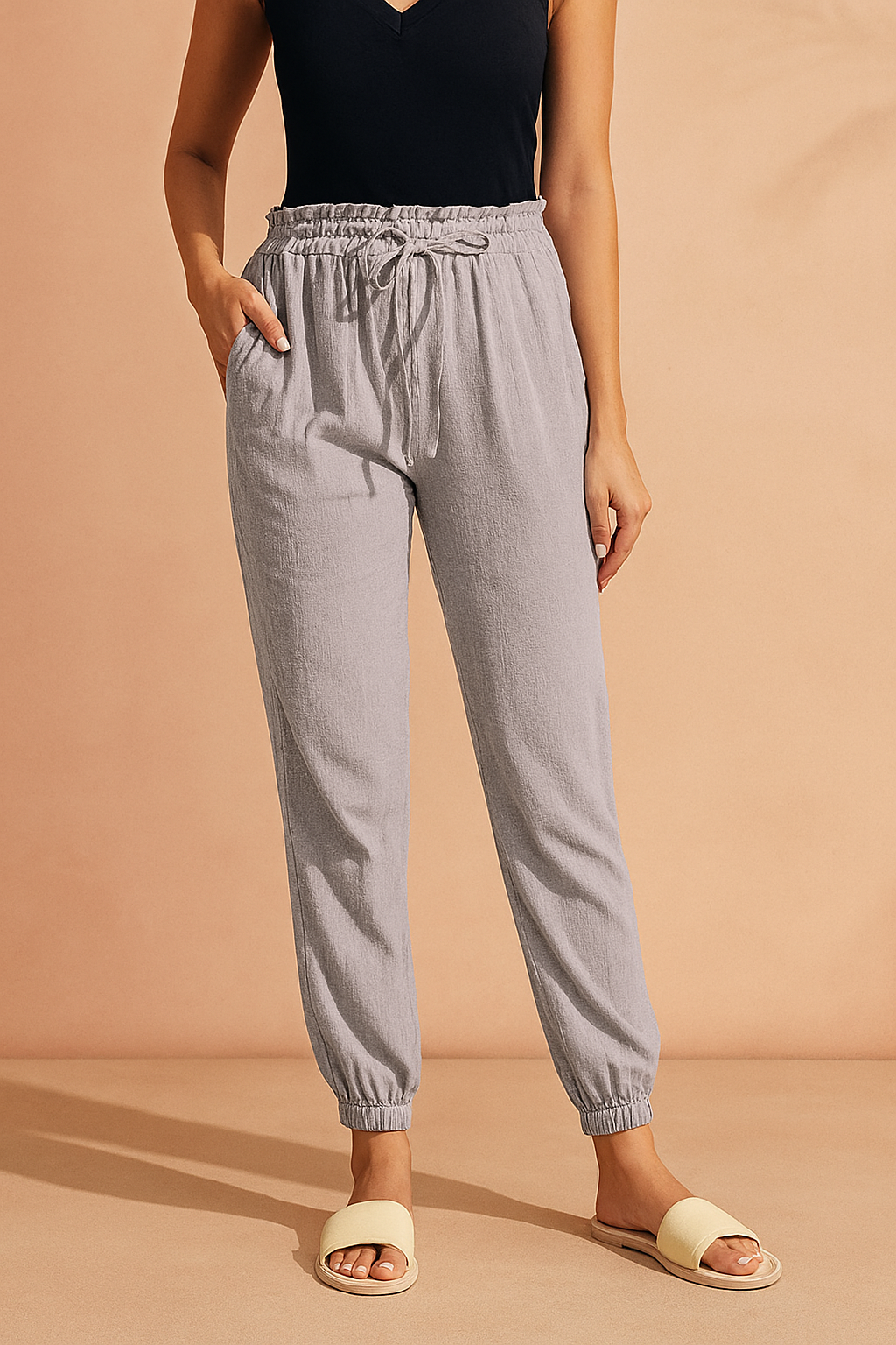 Light gray jogger pants with a textured fabric, drawstring waist, side pockets, and elasticated cuffs, styled with a tucked-in black sleeveless top and beige slide sandals.