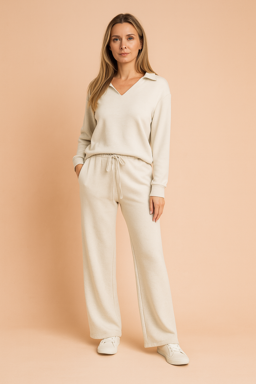 Off-white lounge set featuring a V-neck pullover with a collar and matching wide-leg drawstring pants made from soft knit fabric, styled with minimal white sneakers.