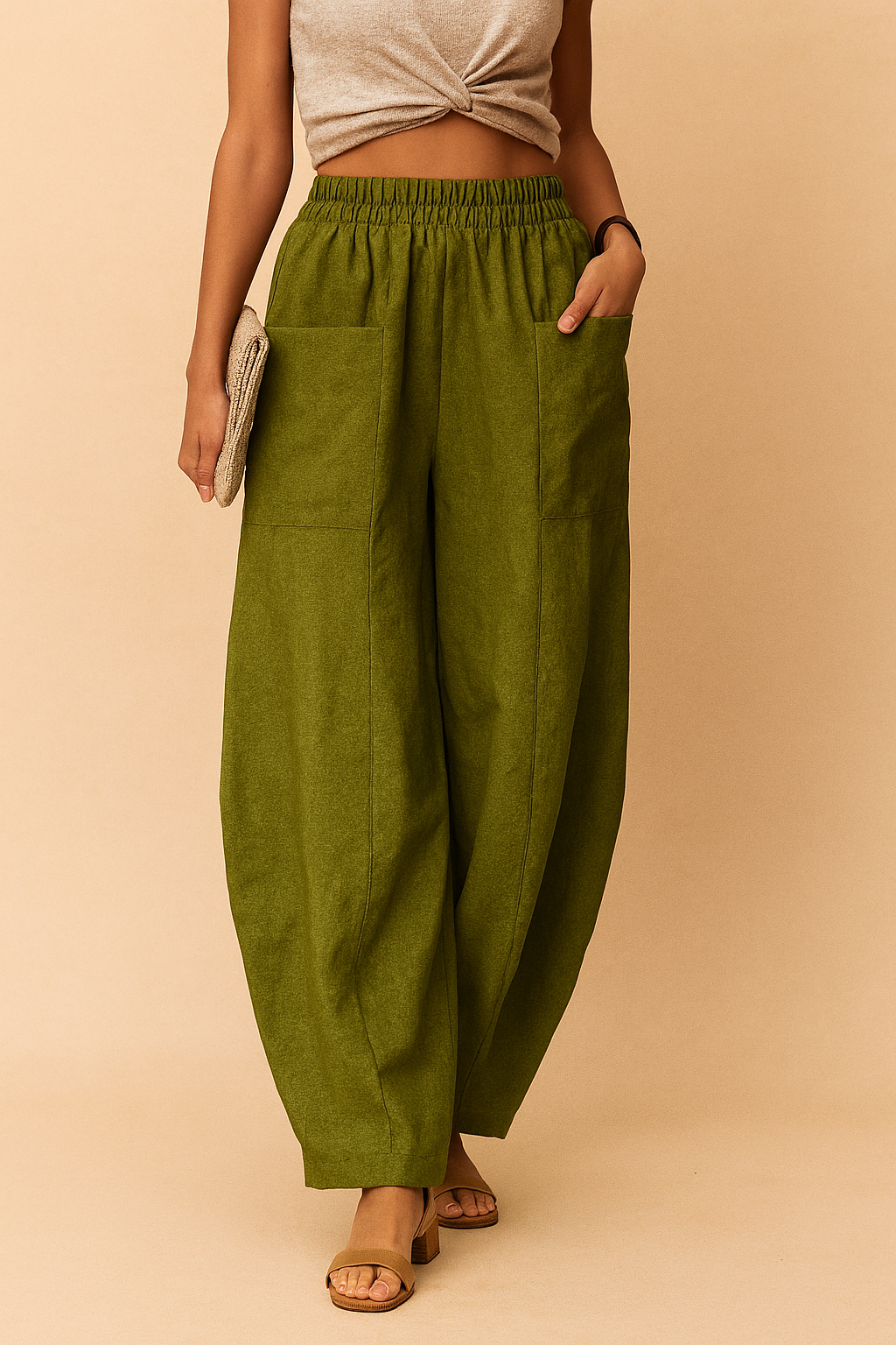 High-waisted olive green linen pants with oversized front patch pockets, wide-leg cut, subtle front seam detailing, and an elastic waistband, styled with open-toe block-heeled sandals.