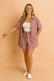 Two-piece coord set featuring a button-up shirt with patch pocket and matching drawstring shorts, both in a soft pink tone with a breezy, relaxed fit and textured finish.