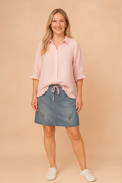 Light pink button-up blouse with ruffled hem and cuffs, paired with a blue denim skirt featuring subtle floral embroidery.