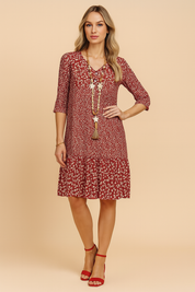 Sukienka boho w kolorze ceglanej czerwieni z białym drobnym wzorem kwiatowym, dekoltem w serek, rękawami 3/4, ozdobnymi guzikami i rozkloszowanym dołem z falbaną, wykonana z lekkiej, zwiewnej tkaniny.