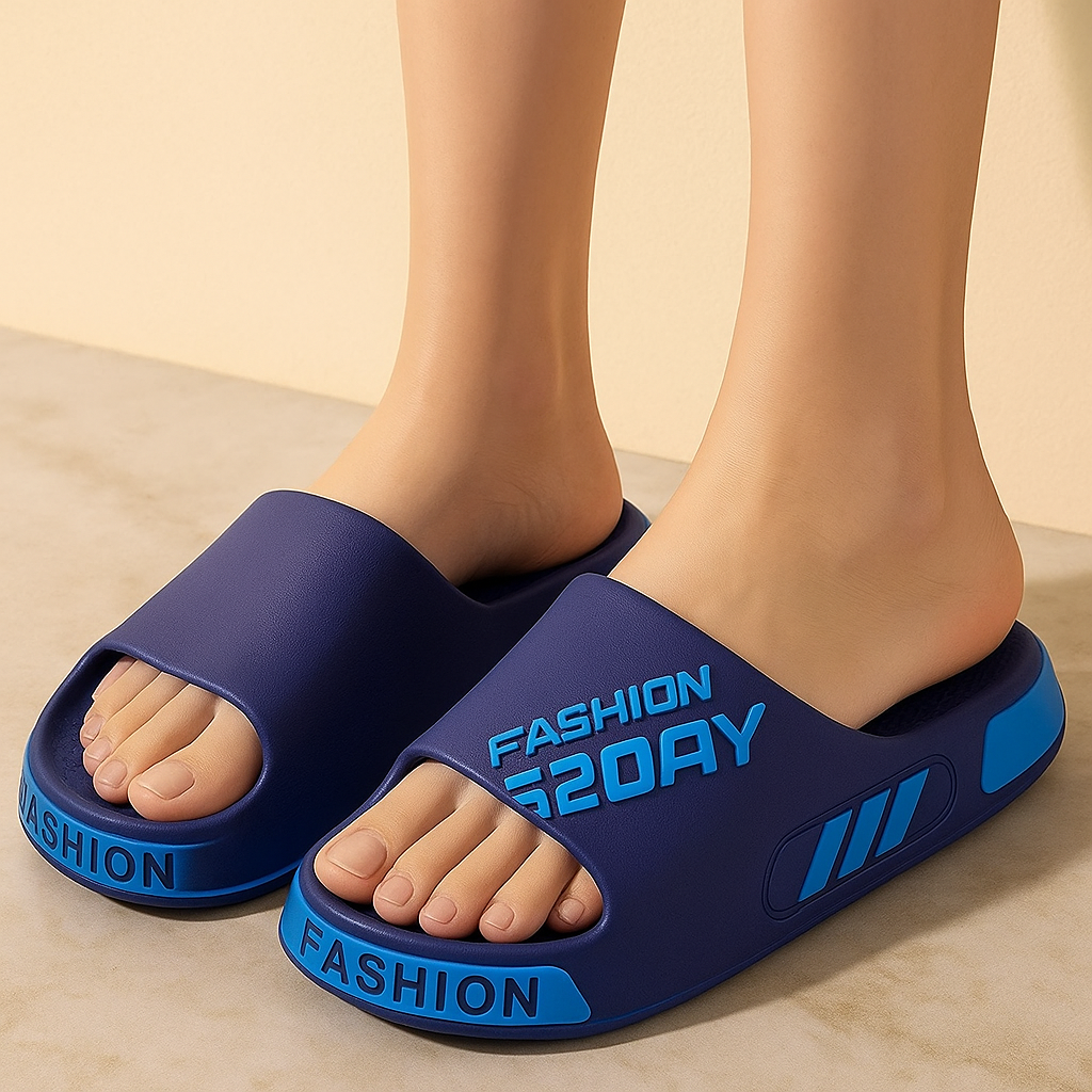 Granatowe klapki kąpielowe z niebieskimi detalami i napisem „FASHION S20AY”, wykonane z piankowego tworzywa, prezentowane na stopach modelki na tle jasnobeżowej ściany i podłogi z ciepłego kamienia.