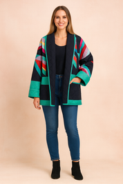 Colorful quilted kimono-style jacket with bold geometric multicolor stripes on a black base, finished with green quilted panels and trim, paired with black leggings and ankle boots.