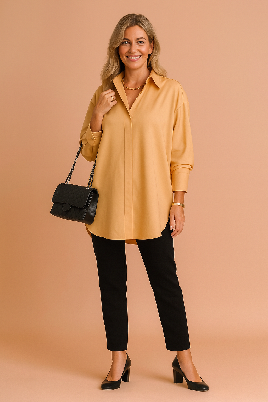 Mustard yellow oversized long-sleeve blouse with a clean collar and concealed front placket, paired with fitted black trousers and black block-heeled pumps; completed with a quilted black chain-strap handbag.