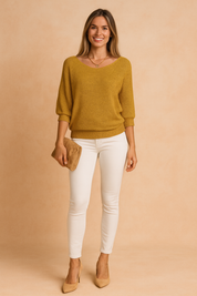 Mustard yellow knit sweater with a relaxed fit and ribbed cuffs, paired with high-waisted white skinny jeans and beige pointed-toe heels, accessorized with a small tan suede clutch and a delicate gold necklace.