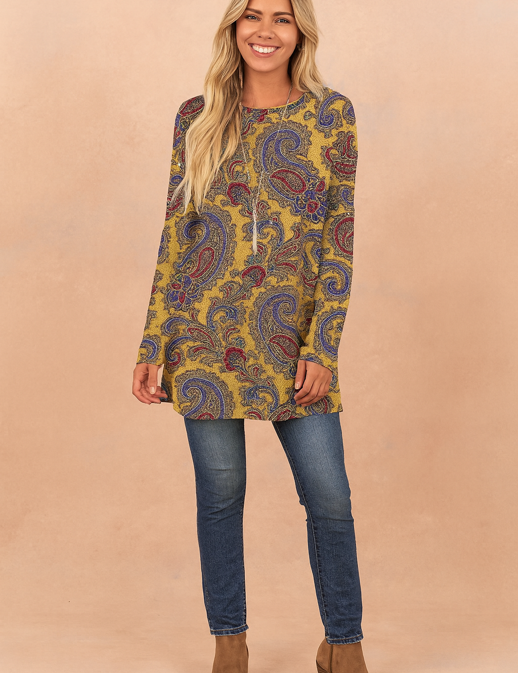 Mustard yellow paisley print long-sleeve tunic top with a relaxed fit, paired with dark blue skinny jeans and tan suede ankle boots.