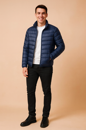 Navy blue lightweight puffer jacket with horizontal quilting, front zipper closure, and stand-up collar, styled with slim-fit black pants and black leather boots.