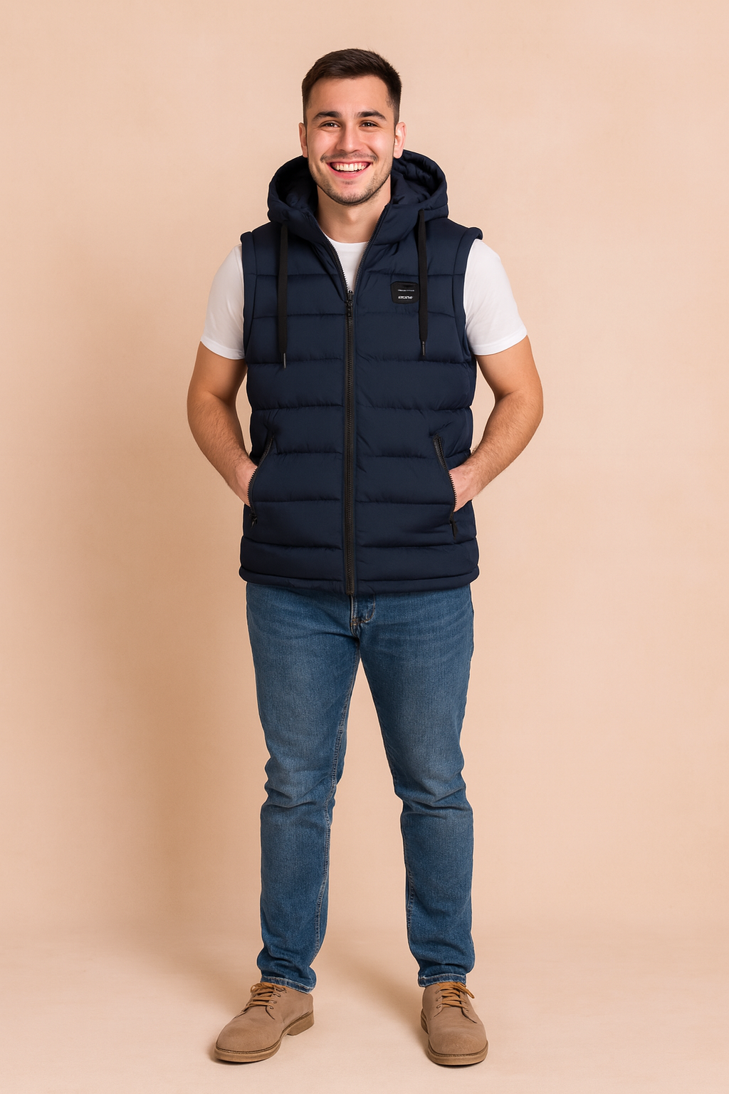 Men’s navy blue sleeveless padded vest with hood, front zipper closure, and two side zip pockets, styled over a white t-shirt and dark denim jeans.