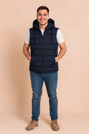 Men’s navy blue sleeveless padded vest with hood, front zipper closure, and two side zip pockets, styled over a white t-shirt and dark denim jeans.