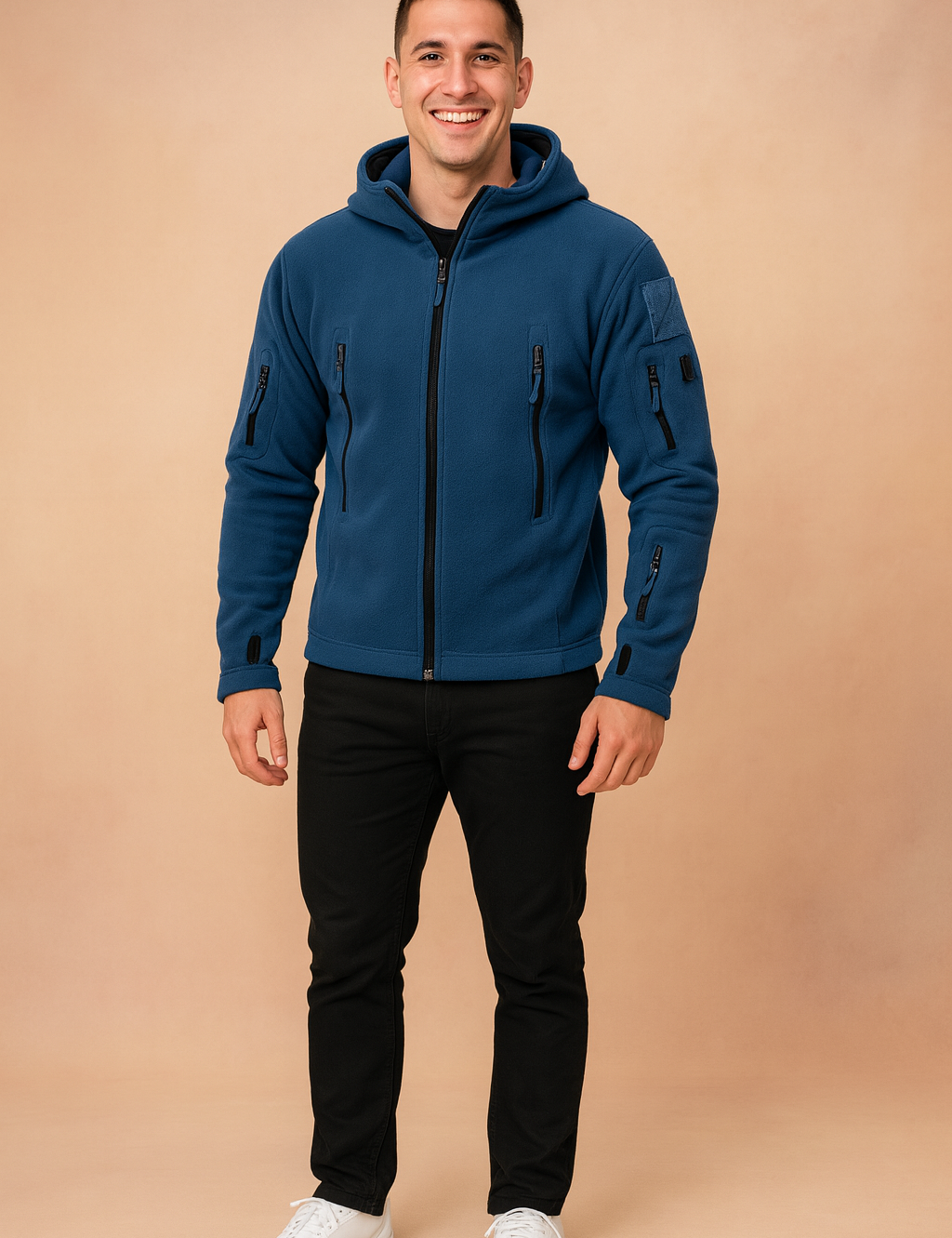 Navy blue softshell tactical jacket with multiple zippered pockets and hood, styled with black trousers and white sneakers.