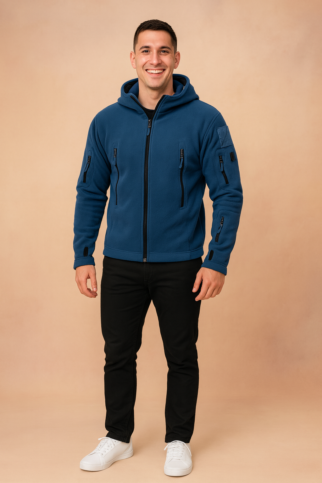 Navy blue softshell tactical jacket with multiple zippered pockets and hood, styled with black trousers and white sneakers.