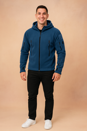 Navy blue softshell tactical jacket with multiple zippered pockets and hood, styled with black trousers and white sneakers.