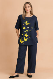 Two-piece navy blue cotton set featuring a half-sleeve top with bright yellow butterfly prints cascading down the front and matching wide-leg pants with minimal seam detailing.