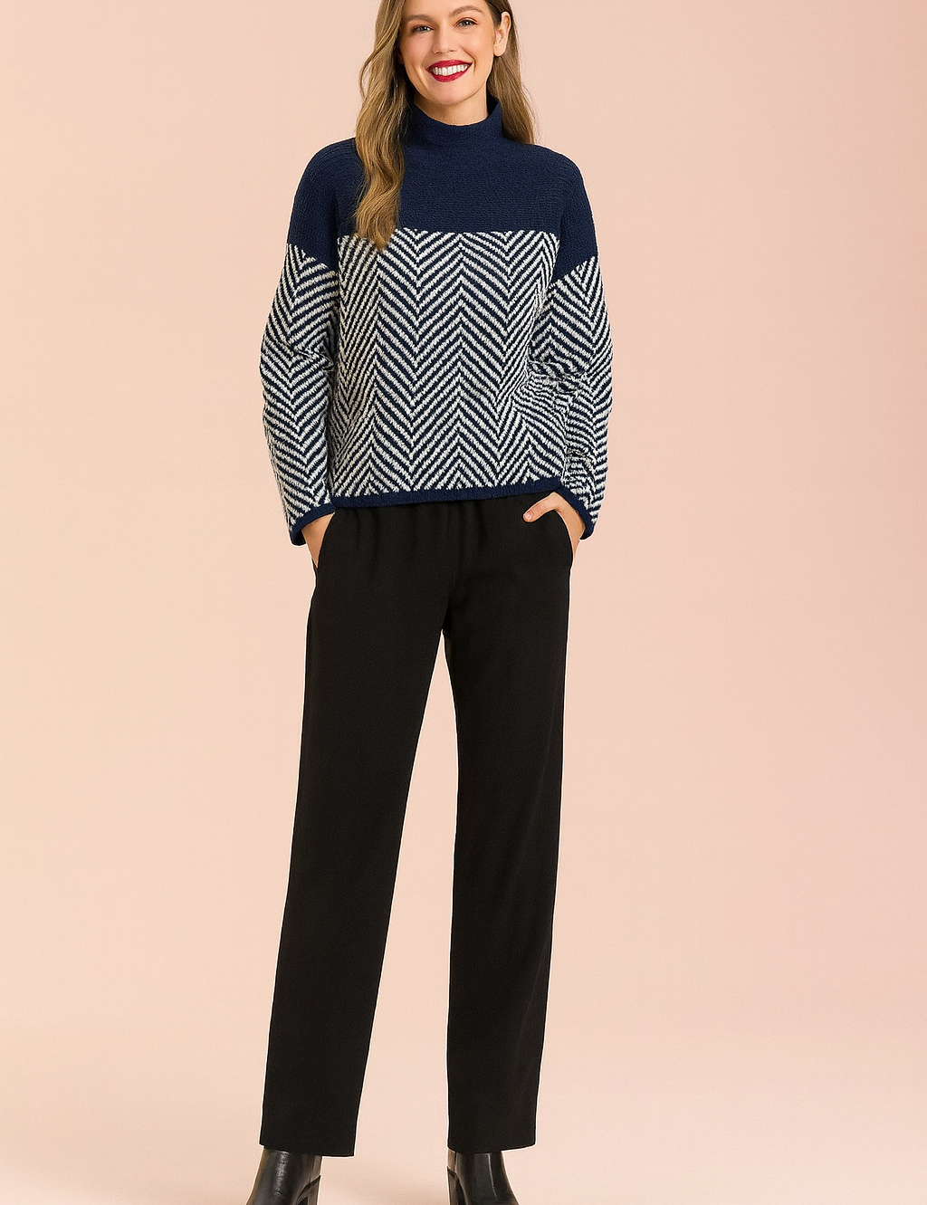 Navy and white chevron-patterned knit sweater with solid navy upper panel, paired with straight-leg black trousers and black ankle boots.