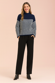Navy and white chevron-patterned knit sweater with solid navy upper panel, paired with straight-leg black trousers and black ankle boots.