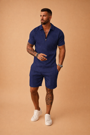 Navy blue two-piece men’s summer set featuring a short-sleeve polo shirt and matching tailored shorts with a subtle geometric jacquard pattern, textured fabric finish, clean seams, modern athletic cut, and paired with minimalist white low-top sneakers for a refined casual look