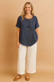 Navy blue short-sleeve linen blouse featuring a round neckline and asymmetrical wooden button detailing down the front, styled with off-white wide-leg pants.
