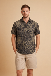 Navy blue short-sleeve button-up shirt with intricate paisley floral pattern in beige, gold, and burnt orange tones, paired with tailored beige knee-length chino shorts.