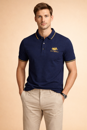 Navy blue short-sleeve polo shirt with structured collar, yellow contrast piping, embroidered crest logo on chest, and classic three-button placket, paired with beige straight-leg chinos featuring a clean tailored fit.