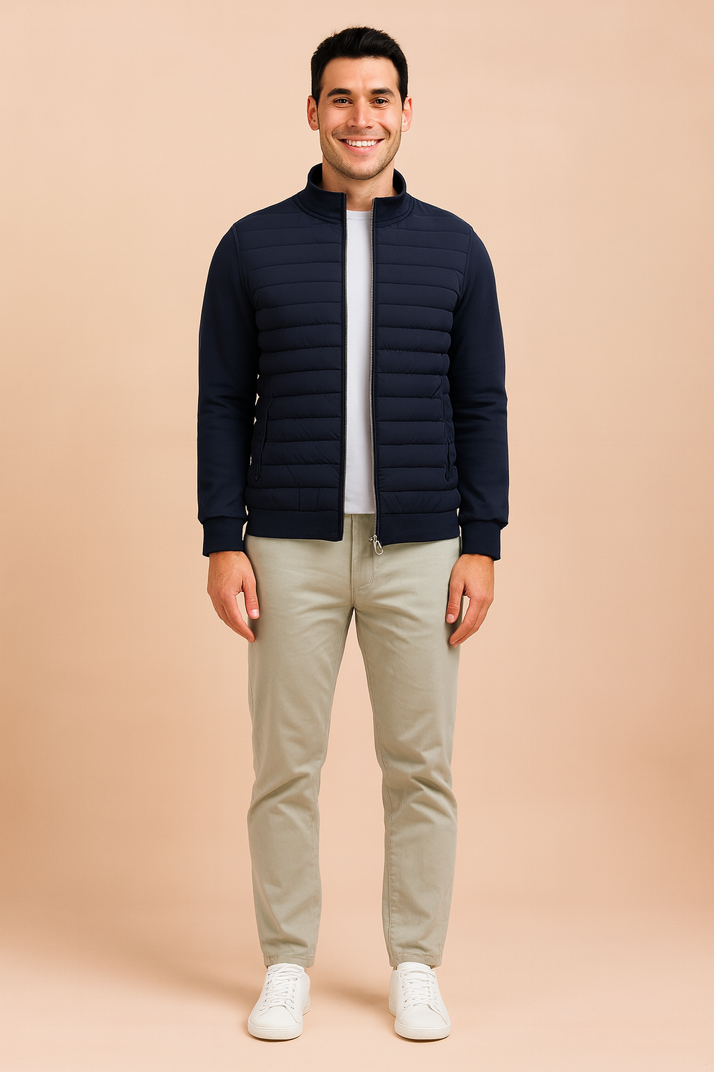 Navy blue quilted zip-up jacket with ribbed cuffs, horizontal padded front detailing, and side pockets, styled over a white shirt and paired with light trousers.