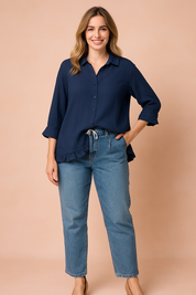 Navy blue long-sleeve button-up blouse with a classic collar, loose silhouette, and playful ruffled hem and cuffs, styled over light-wash denim.
