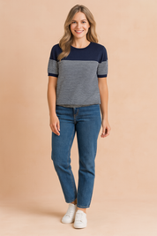 Short-sleeve navy blue and white striped knit top with solid navy shoulders and neckline, paired with medium-wash straight-leg jeans and white sneakers.