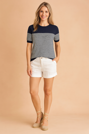 Short-sleeve navy knit top with fine horizontal white stripes and ribbed cuffs, paired with white high-waisted cuffed shorts.