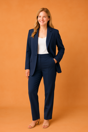 Navy-blue tailored blazer and straight-leg trousers styled with a white tank top and nude heels, worn by a blonde model on an orange sandy backdrop.