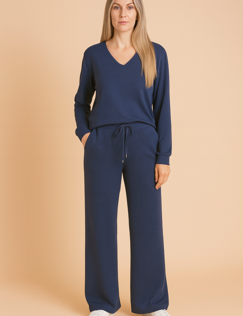Two-piece navy blue loungewear set featuring a long-sleeve V-neck top and wide-leg drawstring pants made from soft jersey fabric, styled with white sneakers.