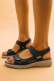 Navy blue open-toe sandals with cut-out detailing, white stitching, silver-tone Velcro straps, and cushioned beige wedge soles.