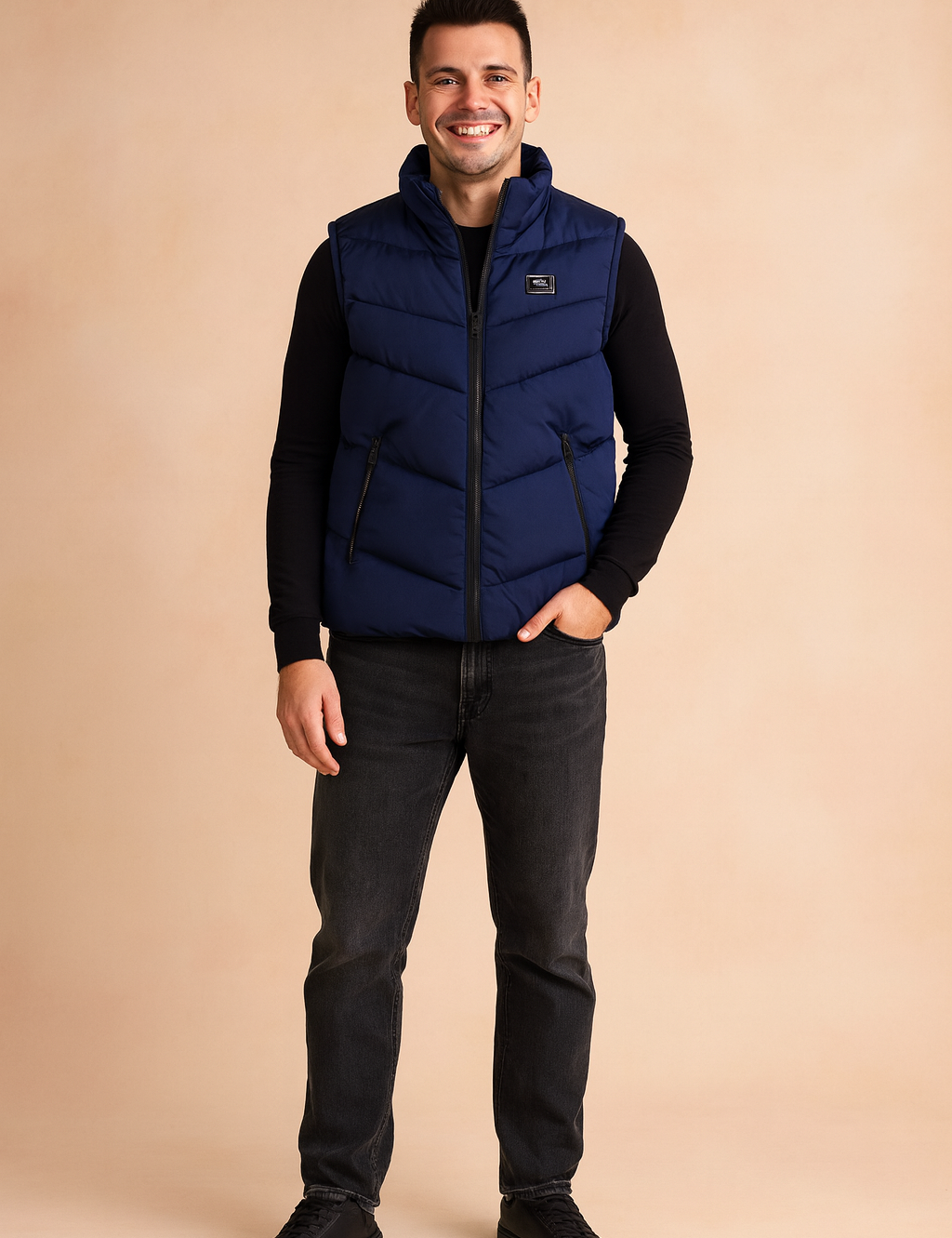 Navy blue puffer vest with chevron quilting, zip closure, and black side pockets, paired with a fitted black long-sleeve shirt and dark jeans for a casual winter
