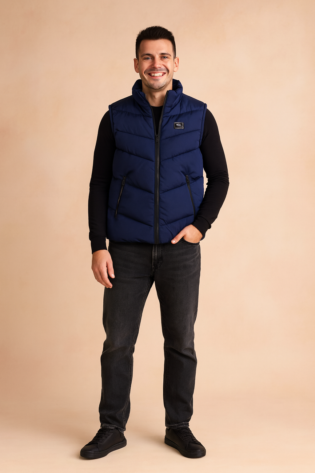 Navy blue puffer vest with chevron quilting, zip closure, and black side pockets, paired with a fitted black long-sleeve shirt and dark jeans for a casual winter