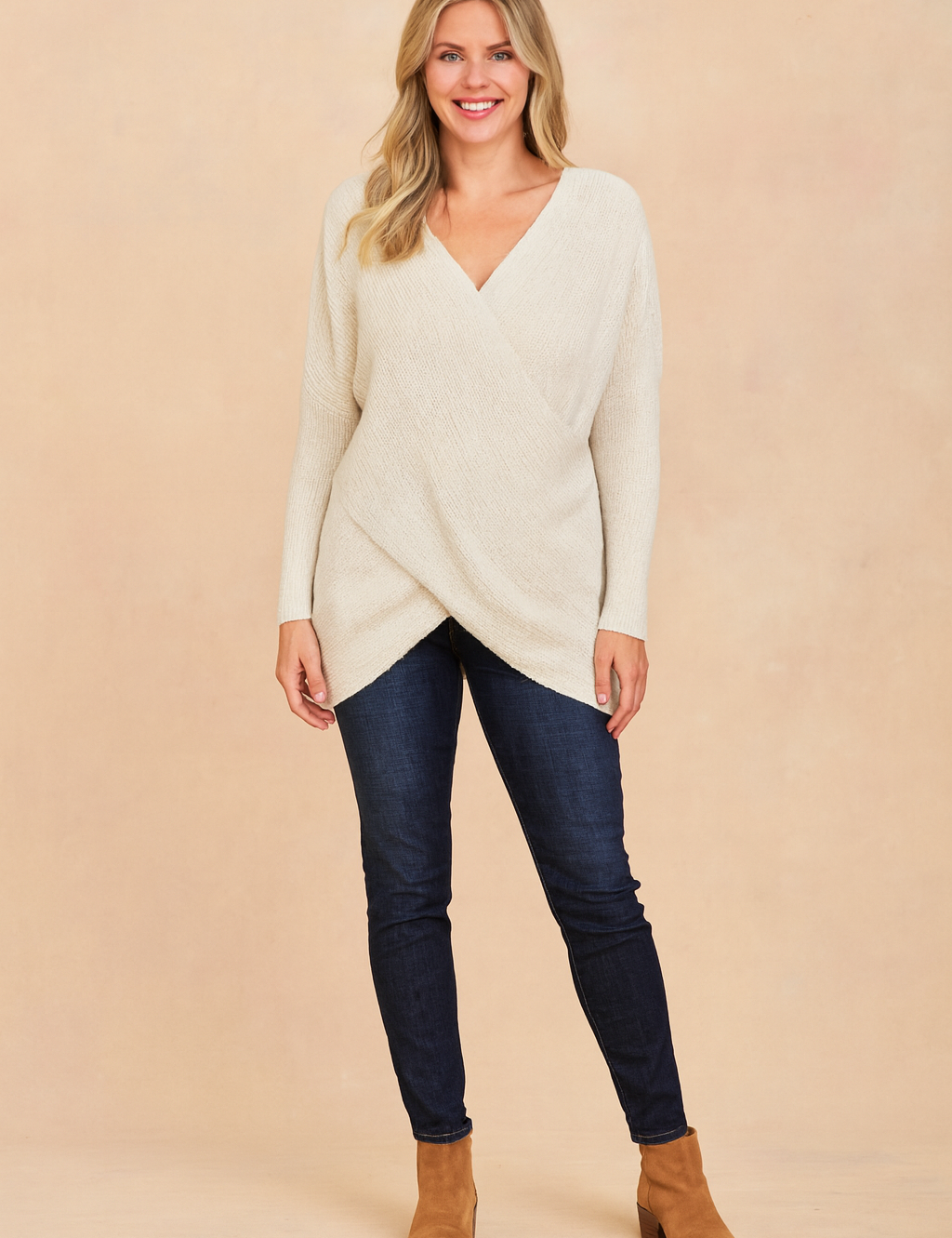 Off-white textured knit crossover sweater with asymmetrical hem, paired with dark-wash skinny jeans and tan suede ankle boots.
