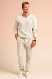Off-white textured knit V-neck sweater paired with light beige drawstring linen pants and white low-top sneakers, styled with a black wristwatch and beaded bracelet.